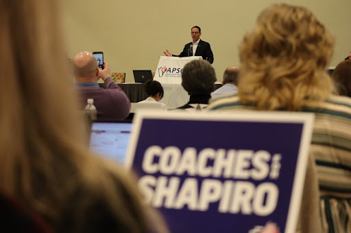 JDS speaking at a conference with a "Coaches for Shapiro" sign in the foreground