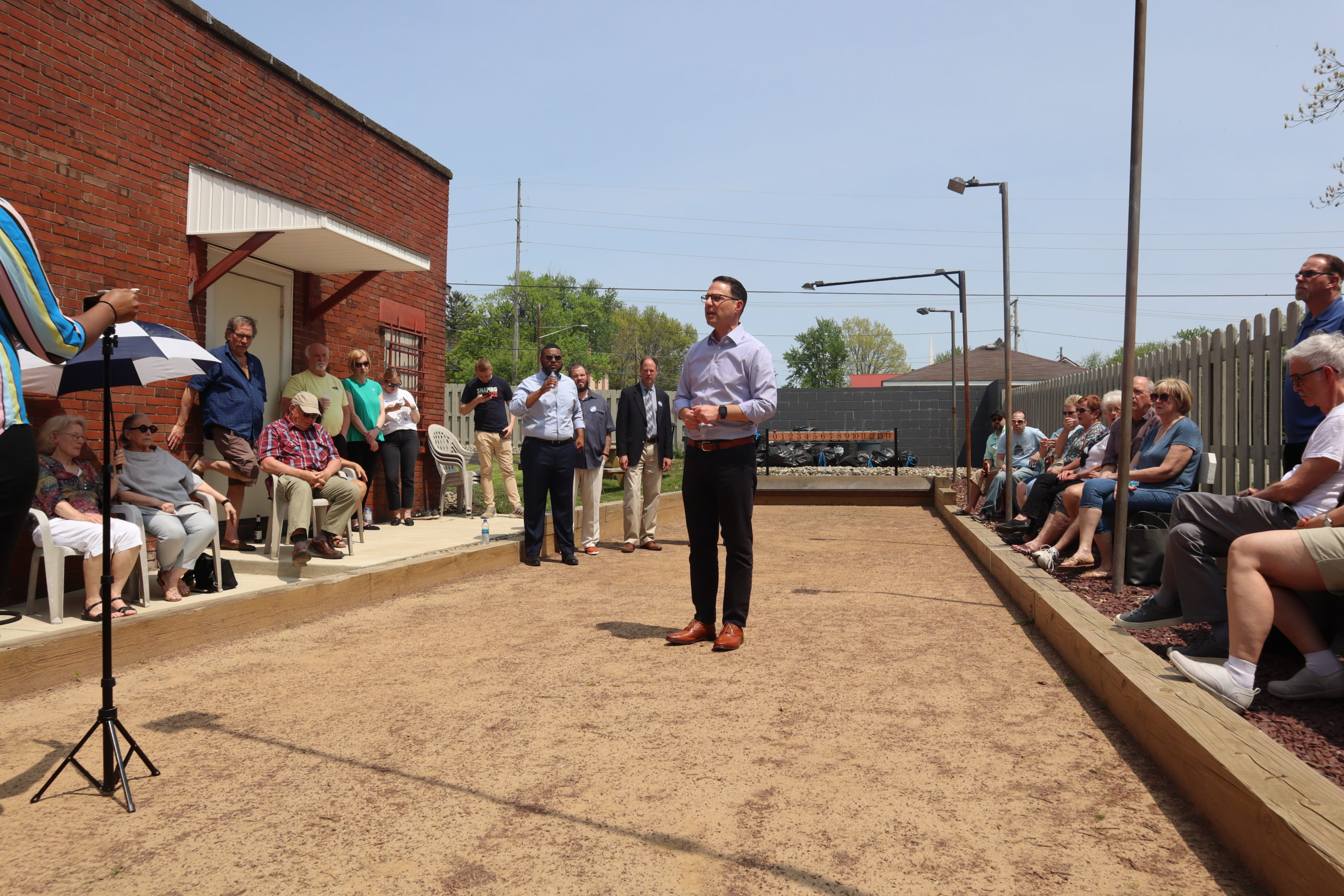 Josh stands in a bocce ball pit giving a speech.