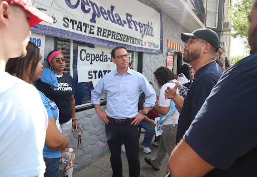 Josh stands in a group of supporters with his hands on his hips.