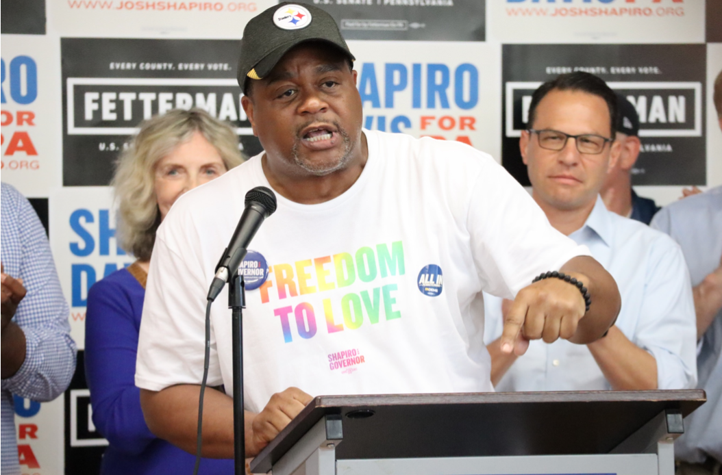 Ed Gainey speaking at a podium wearing a "freedom to love" shirt